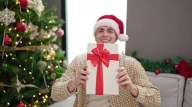 Evde kendine güvenen genç İspanyol adam Noel hediyesini tutuyor.