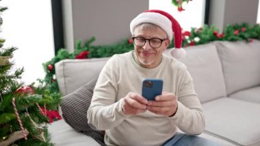 Orta yaşlı, kır saçlı bir adam evde Noel ağacına fotoğraf çeker.