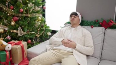 Genç İspanyol adam Noel 'i kutluyor. Kanepede oturuyor. Evde karın ağrısı çekiyor.