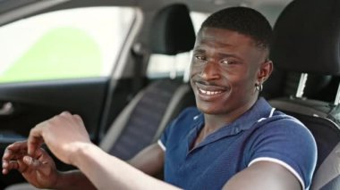 Afro-Amerikalı adam gülümsüyor. Sokakta kendinden emin araba kullanıyor.