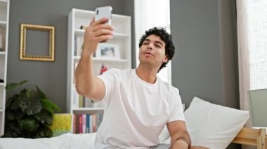 Genç latin adam yatak odasındaki yatakta video görüşmesi yapıyor.