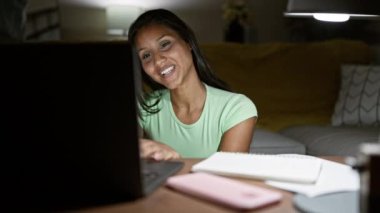 Genç Latin kadın video görüşmesi yapıyor. Evde not alıyor.