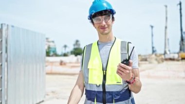 Genç İspanyol mimar elinde telsizle inşaat alanında el hareketi yapıyor.