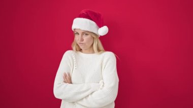 Genç, sarışın, üzgün, izole kırmızı arka planda Noel şapkası takan bir kadın.