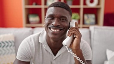 Afro-Amerikalı adam telefonda konuşuyor. Kanepede oturuyor ve gülümsüyor.
