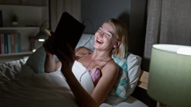 Genç sarışın kadın yatak odasında film izlerken çok gülüyor.
