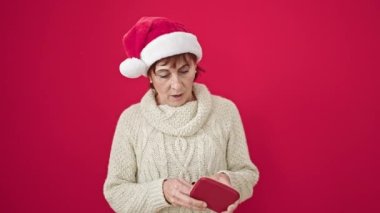 Olgun İspanyol kadın Noel şapkası takıyor ve izole edilmiş kırmızı arka planda boş cüzdana bakıyor.