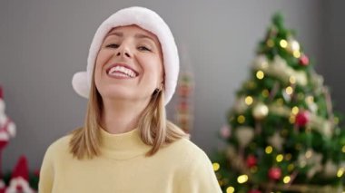 Evde Noel ağacının yanında kendinden emin gülümseyen genç sarışın kadın.