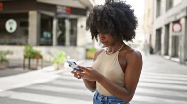 Afro-Amerikalı kadın sokakta akıllı telefon kullanıyor.