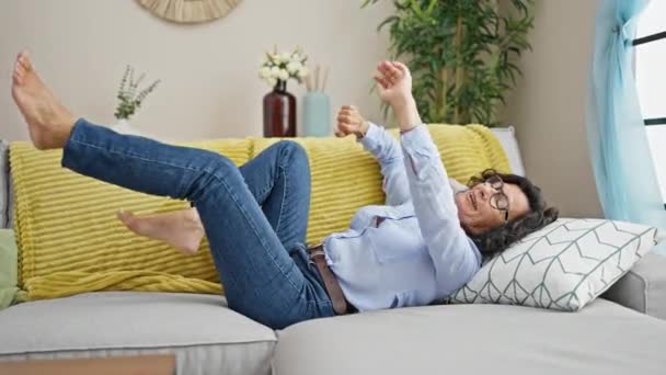 中年のヒスパニック系女性 自宅のソファーに横たわる笑顔 — ストック動画