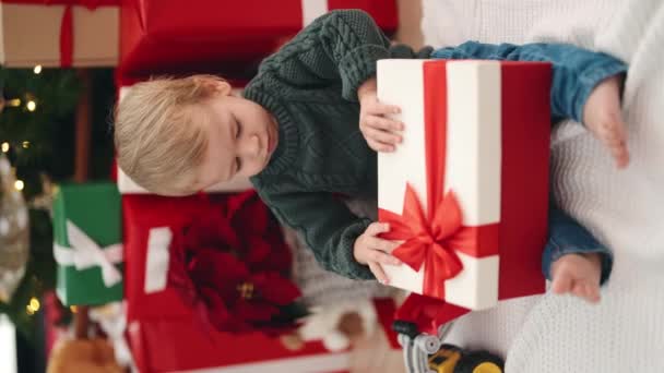 愛らしいブロンドの幼児アンパッキングクリスマスプレゼント自宅で床に座って — ストック動画