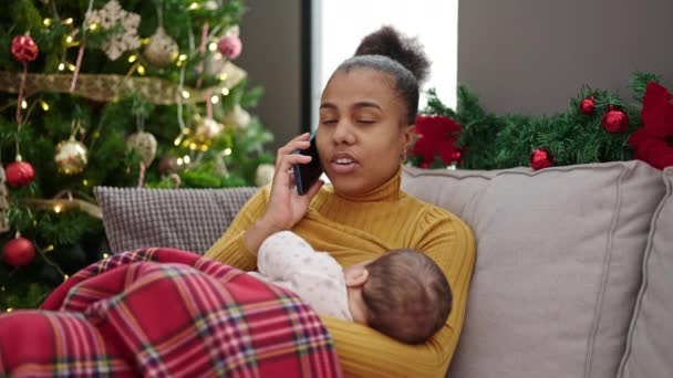 母亲和儿子在家里一边用智能手机庆祝圣诞节一边用母乳喂孩子 — 图库视频影像