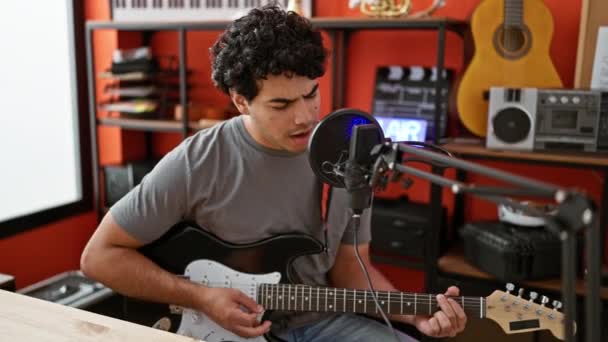 音楽スタジオでエレクトリックギターを演奏する歌を歌う若いラテン人男性ミュージシャン — ストック動画