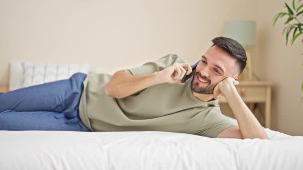 寝室でベッドに横たわっているスマートフォンで話している若いヒスパニックの男 — ストック動画