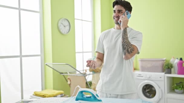 Νεαρός Ισπανόφωνος Μιλάει Smartphone Καύση Ρούχα Σιδέρωμα Στο Δωμάτιο Πλυντηρίων — Αρχείο Βίντεο