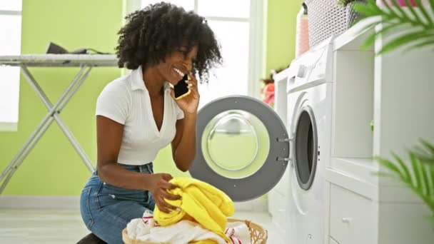 Afroamerikanerin Spricht Auf Smartphone Und Wäscht Lächelnd Wäsche Waschküche — Stockvideo