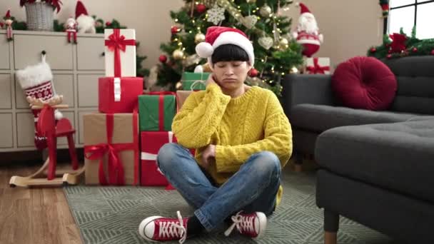 自宅で退屈な表現でクリスマスツリーに座っている若い中国人女性 — ストック動画