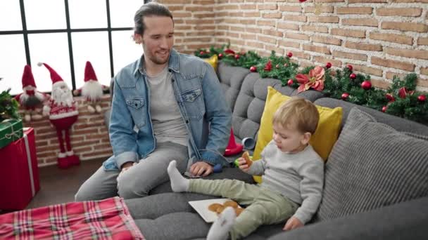 自宅でクリスマスを祝うクッキーを食べる父と息子 — ストック動画