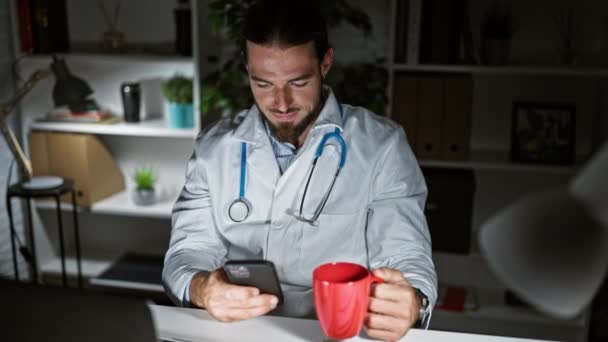 Jovem Hispânico Homem Médico Usando Smartphone Beber Café Trabalhando Clínica — Vídeo de Stock