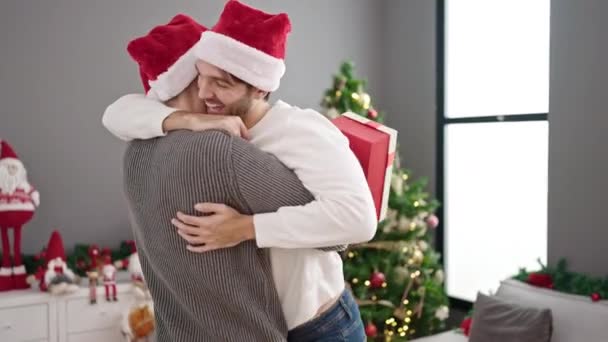 Dwóch Mężczyzn Świętuje Boże Narodzenie Trzymając Prezent Przytulając Się Domu — Wideo stockowe