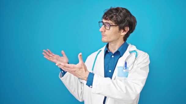 Joven Médico Hispano Sonriendo Confiado Presentando Sobre Aislado Fondo Azul — Vídeos de Stock