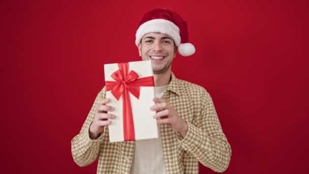Joven Hombre Hispano Sonriendo Confiado Usando Sombrero Navidad Sosteniendo Regalo — Vídeo de stock