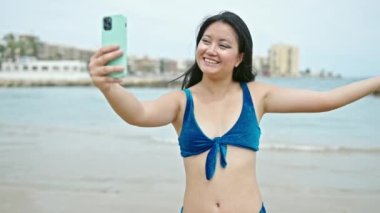 Bikini giyen Çinli genç bir turist kumsalda video görüşmesi yapıyor.