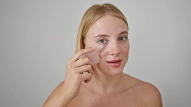 Genç sarışın kadın pembe kuvars gua kullanarak yüz masajı yapıyor.