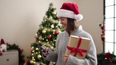 Genç ve güzel İspanyol kadın akıllı telefon kullanıyor. Yılbaşı ağacının yanında duruyor.