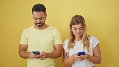Kadın ve erkek, sarı arka planda akıllı telefonlar kullanarak gülümsüyor.