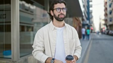 Latin kökenli genç adam kahve içiyor, saati arıyor ve caddede yürüyor.