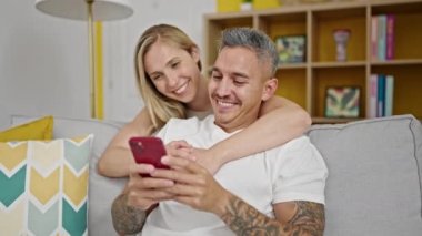 Man and woman couple using smartphone sitting on sofa at home