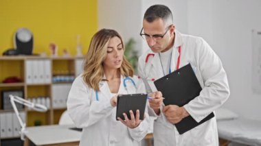 Kadın ve erkek doktorlar klinikte dokunmatik bez kullanarak tıbbi rapor tutuyorlar.