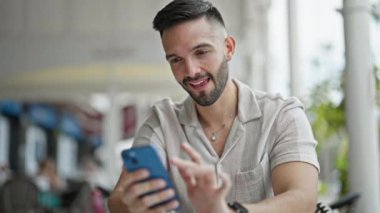 Genç İspanyol adam akıllı telefon kullanıyor. Kahve dükkanının terasında birinci sınıf bir jestle masada oturuyor.