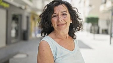 Orta yaşlı İspanyol kadın sokakta kendine güvenerek gülümsüyor.