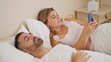 Erkek arkadaş yatak odasında uyurken, kadın ve erkek kız arkadaş akıllı telefon kullanıyor.