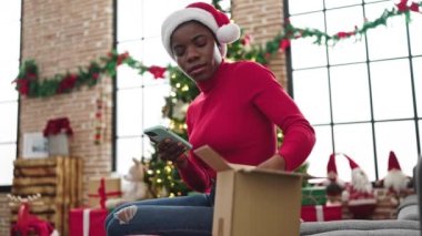 Afrika kökenli Amerikalı bir kadın Noel hediyesini açıyor ve evde fotoğraf çekiyor.
