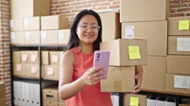Genç Çinli kadın ecommerce işçisi. Ofiste akıllı telefon paketleri tutuyor.