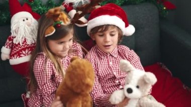 Erkek ve kız kardeş evdeki Noel süslemeleriyle birlikte kanepede oyuncak ayılarla oynuyorlar.