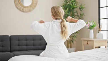 Genç sarışın kadın yatak odasında kollarını esneterek uyanıyor.