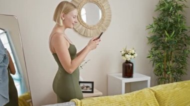 Evdeki kanepede uzanmış akıllı telefon kullanan genç sarışın kadın.