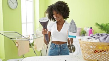 Afrika kökenli Amerikalı kadın çamaşır odasında ütü makineleri arasında seçim yapıyor.
