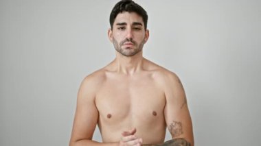 Genç İspanyol adam gülümsüyor. Üstsüz, soyutlanmış beyaz arka planda duruyor.