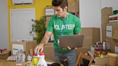 Genç İspanyol gönüllü yardım merkezinde dizüstü bilgisayar kullanarak ürünleri kontrol ediyor.