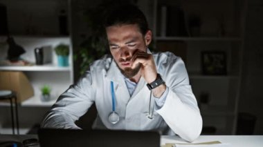 Genç İspanyol doktor dizüstü bilgisayar kullanıyor. Klinikte esnemekten yoruldu.