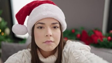 Genç, güzel İspanyol bir kadın evdeki Noel ağacının yanındaki koltukta video görüşmesi yapıyor.