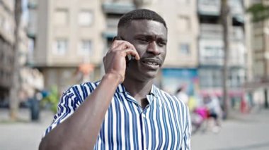 Afro-Amerikalı adam gülümsüyor. Kendine güveniyor. Akıllı telefondan konuşuyor.