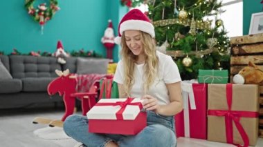 Genç sarışın kadın Noel şapkası takıyor hediyesini açıyor ve üzgün görünüyor.