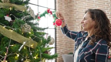 Orta yaşlı İspanyol kadın Noel ağacını evde süslüyor.