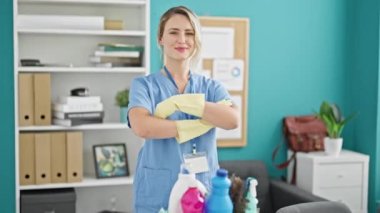 Genç sarışın kadın profesyonel temizlikçi kollarını kavuşturup ofiste duruyor.
